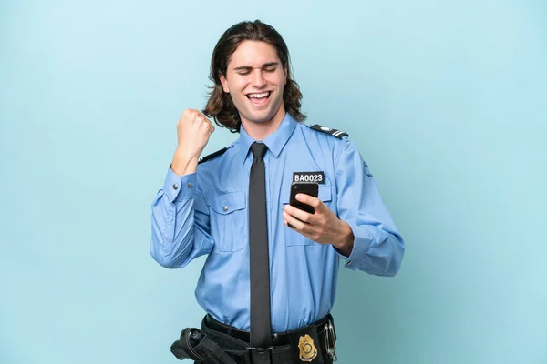 Young police caucasian man isolated on blue background with phone in victory position