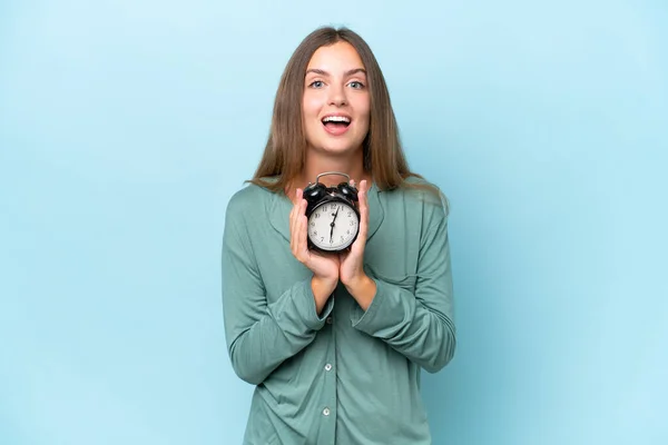 Young Beautiful Woman Isolated Blue Background Pajamas Holding Clock Surprised — Stock Photo, Image