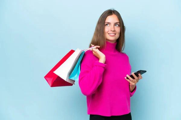 Ung Vacker Kvinna Isolerad Blå Bakgrund Håller Shoppingväskor Och Mobiltelefon — Stockfoto