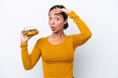 Beyaz arka planda izole edilmiş hamburgerini tutan genç İspanyol kadın yan tarafa bakarken sürpriz jest yapıyor.