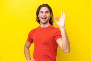 Sarı arka planda izole edilmiş beyaz yakışıklı adam parmaklarıyla tamam işareti gösteriyor.