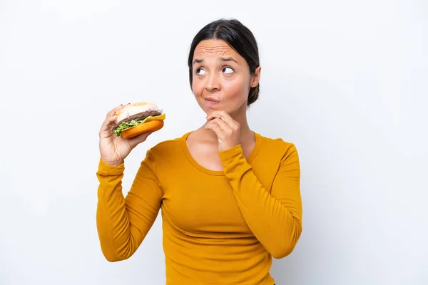 Młoda Latynoska Kobieta Trzyma Hamburgera Białym Tle Mając Wątpliwości Myślenia — Zdjęcie stockowe