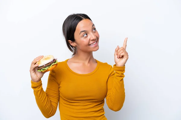 Jonge Spaanse Vrouw Houdt Een Hamburger Geïsoleerd Witte Achtergrond Wijzend — Stockfoto