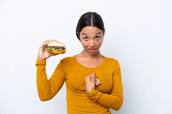 Młoda Latynoska Kobieta Trzyma Hamburgera Białym Tle Zaskakującym Wyrazem Twarzy — Zdjęcie stockowe