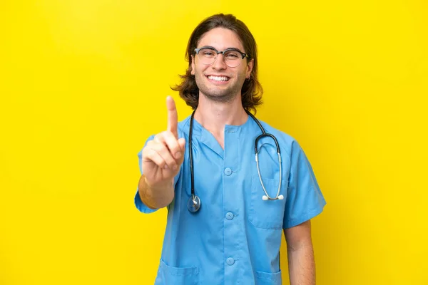 年轻的外科医生在黄色背景下被隔离 露出并举起了一个手指 — 图库照片