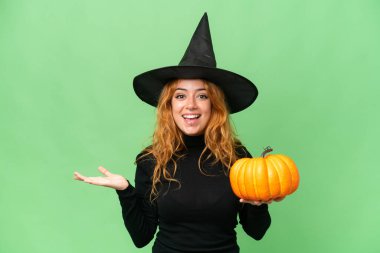 Cadı kostümü giymiş beyaz bir kadın. Elinde bir balkabağı var. Yeşil ekran krom anahtar arka planda ve yüzünde şok ifadesi var.