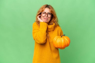 Yeşil ekran krom üzerinde izole edilmiş bir balkabağı tutan genç beyaz kadın hayal kırıklığına uğramış ve kulaklarını kapatmış.