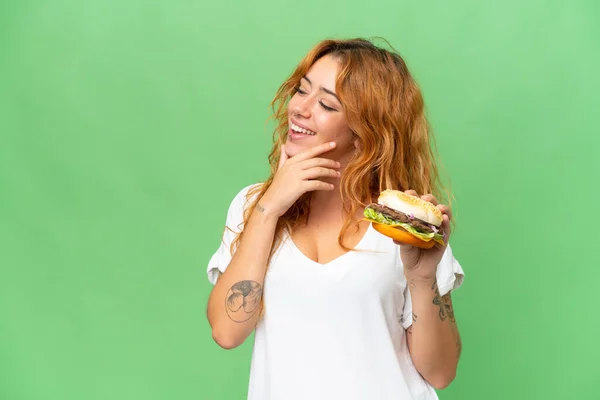 緑の画面に隔離されたハンバーガーを保持若い白人女性クロマキー背景思考アイデアと見て側 — ストック写真