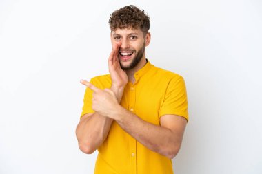 Beyaz arka planda soyutlanmış yakışıklı beyaz bir adam bir ürünü sunmak ve bir şeyler fısıldamak için kenarı işaret ediyor.