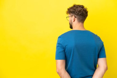 Sarı arka planda izole edilmiş yakışıklı beyaz adam arkasına bakıyor.