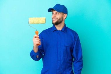 Kafkasyalı ressam mavi arka planda izole edilmiş, yana bakıyor ve gülümsüyor.