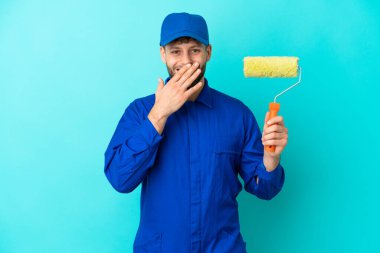 Kafkasyalı ressam mavi arka planda izole edilmiş mutlu ve gülümseyen elleri ile ağzını kapatıyor.
