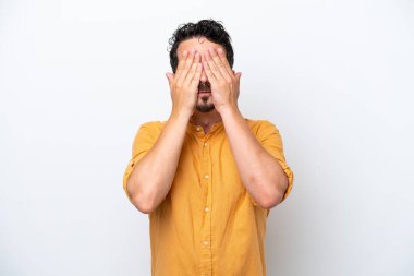 Bıyıklı genç adam, beyaz arka planda, gözleri elleriyle kapatıyor.