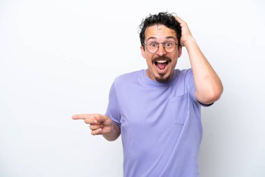 Bıyıklı genç adam beyaz arka planda izole edilmiş, şaşırmış ve işaret ediyor.