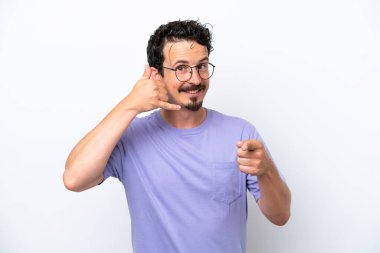 Bıyıklı genç adam beyaz arka planda izole edilmiş telefon hareketleri yapıyor ve ön tarafı işaret ediyor.