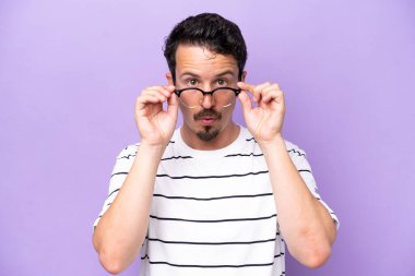 Mor arka planda gözlüklü ve şaşkın bakışlı genç beyaz adam.