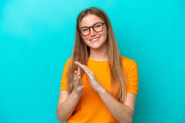 Mavi arka planda izole edilmiş genç beyaz kadın bir konferanstan sonra alkışlıyor.