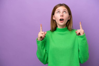 Mor arka planda izole edilmiş genç bir İngiliz kadın şaşırmış ve işaret ediyor.