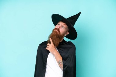 Cadılar bayramında genç büyücü mavi arka planda izole edilmiş ve yukarı bakıyor