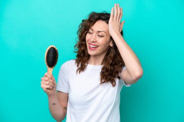 Mavi arka planda saç fırçası tutan genç beyaz kadın bir şeyin farkına vardı ve çözüme niyetlendi.