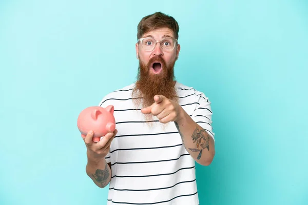 Roodharige Man Met Lange Baard Houdt Een Varkensbank Geïsoleerd Blauwe — Stockfoto