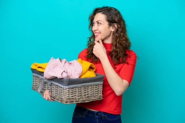 Kafkasyalı genç bir kadın mavi arka planda izole edilmiş bir sepet tutuyor. Yan tarafa bakıyor ve gülümsüyor.