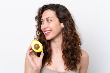 Beyaz arka planda izole edilmiş beyaz bir kadın elinde bir avokado tutarken gülümsüyor. Portreyi kapat