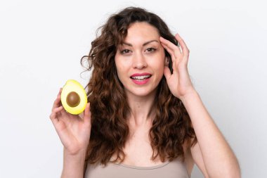 Beyaz arka planda izole edilmiş beyaz bir kadın elinde bir avokado tutarken gülümsüyor. Portreyi kapat