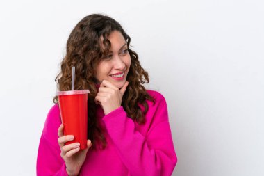 Beyaz arka planda izole edilmiş gazoz içen genç beyaz kadın bir fikir düşünüyor ve bakıyor.