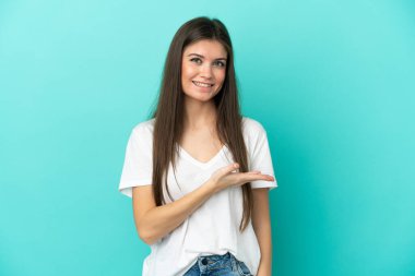 Mavi arka planda izole edilmiş genç beyaz kadın bir fikir sunuyor ve gülümsüyor.