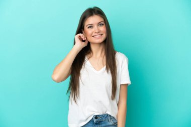 Mavi arka planda izole edilmiş genç beyaz kadın gülüyor.