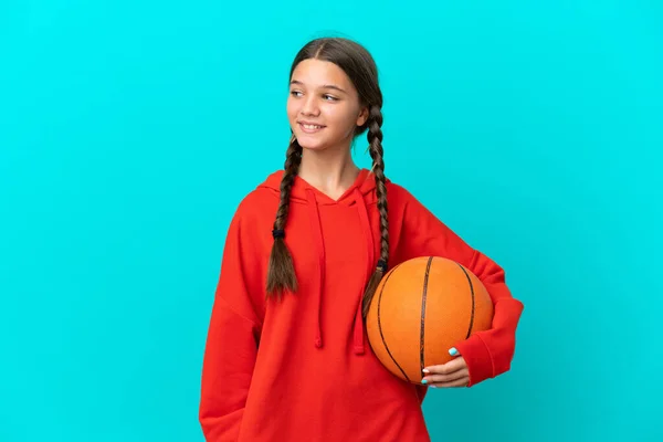 在蓝色背景下孤零零地打篮球的高加索小女孩望着旁边笑着 — 图库照片