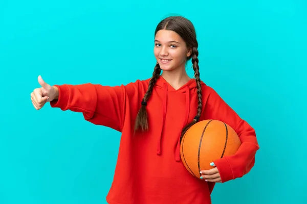一个被蓝色背景隔离的小女孩打篮球 她举起了一个大拇指 — 图库照片