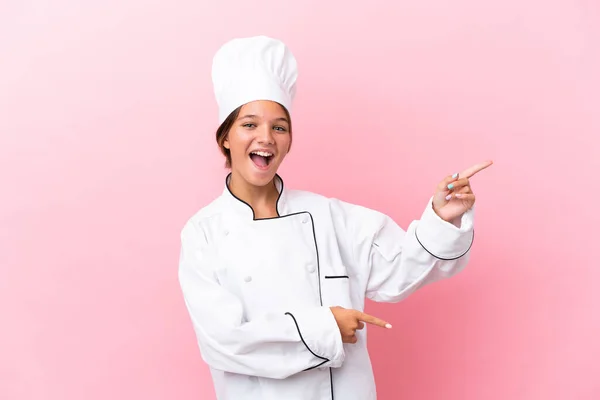 Pouco Caucasiano Chef Menina Isolado Fundo Rosa Surpreendido Apontando Lado — Fotografia de Stock