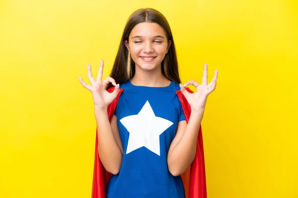 小さいですCaucasianスーパーヒーロー女の子絶縁上の黄色背景でゼンポーズ — ストック写真