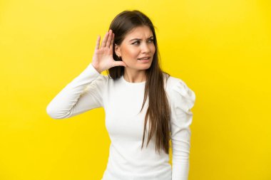Sarı arka planda izole edilmiş genç beyaz bir kadın. Kulağına elini sürerek bir şeyler dinliyor.