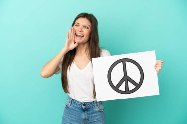 Kafkasyalı genç bir kadın mavi arka planda izole edilmiş. Elinde barış sembolü ve bağıran bir levha var.