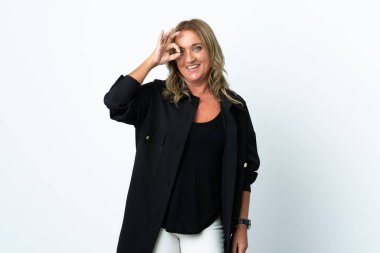 İzole edilmiş beyaz arka planda orta yaşlı sarışın kadın parmaklarıyla tamam işareti gösteriyor.