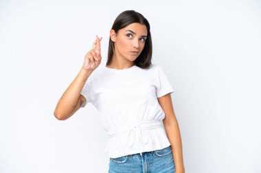 Beyaz arka planda izole edilmiş beyaz tenli genç bir kadın parmaklarını çapraz yapıp en iyisini diliyor.