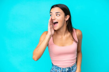 Mavi arka planda izole edilmiş genç beyaz kadın ağzı sonuna kadar açık bağırıyor.