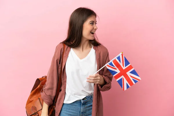 年轻的高加索女人举着一面英国国旗 与粉色背景隔离 横向笑着 — 图库照片