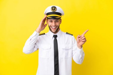 Kafkasyalı uçak pilotu sarı arka planda izole edildi. Şaşırdı ve işaret etti.