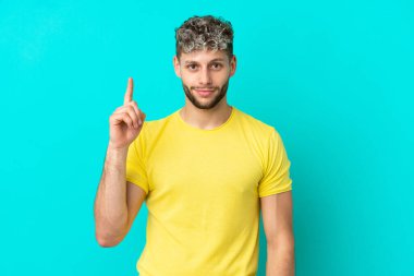 Mavi arka planda izole edilmiş yakışıklı beyaz adam harika bir fikre işaret ediyor.