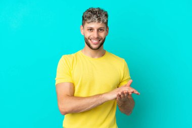 Mavi arka planda izole edilmiş yakışıklı beyaz adam alkışlıyor.