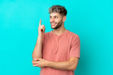 Mavi arka planda izole edilmiş yakışıklı beyaz adam harika bir fikre işaret ediyor.