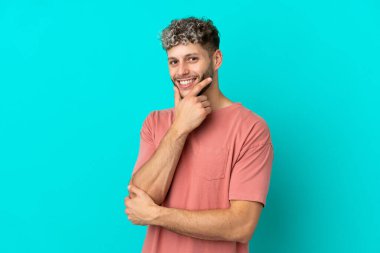 Mavi arka planda izole edilmiş yakışıklı beyaz adam mutlu ve gülümsüyor.