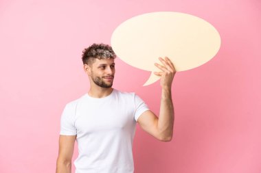 Pembe arka planda izole edilmiş yakışıklı beyaz adam boş bir konuşma balonu tutuyor.
