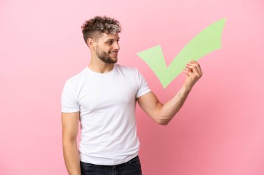Pembe arka planda izole edilmiş yakışıklı beyaz bir adam elinde mutlu bir ifadeyle bir çek simgesi tutuyor.