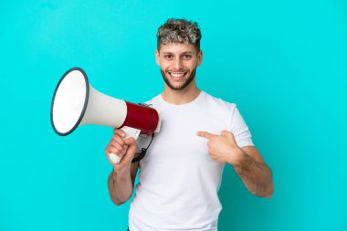 Young handsome caucasian man isolated on blue background holding a megaphone and with surprise facial expression