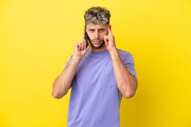 Sarı arka planda izole edilmiş cep telefonu kullanan genç beyaz bir adam bir fikir düşünüyor.